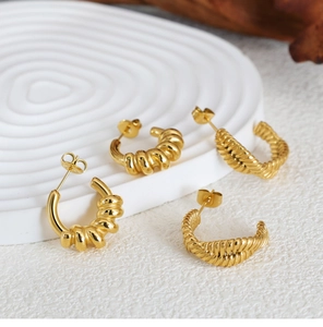 Detailed macro view of gold-plated C-shaped hoop earrings with twisted and woven textures