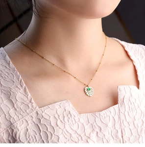 Close-up of gold monstera leaf pendant necklace with green gemstone on model