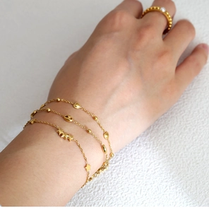 Close-up of layered 18K gold-plated star and heart charm bracelets with pearl ring detail