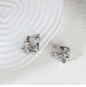 Detail of silver liquid metal earrings with irregular textured surface and glossy finish