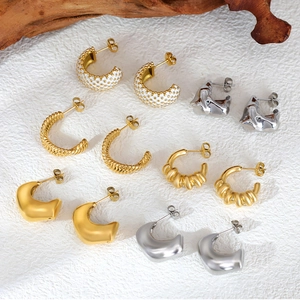 Collection of gold and silver stainless steel C-shape earrings on white stone background