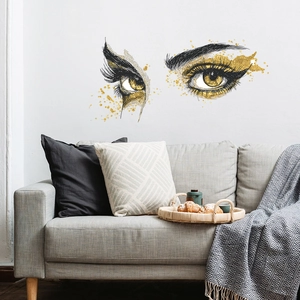 Sticker mural design œil doré et noir au-dessus d'un canapé gris dans un salon moderne