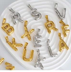 Polished 3D bubble letter pendants in gold and silver finish on a white tray