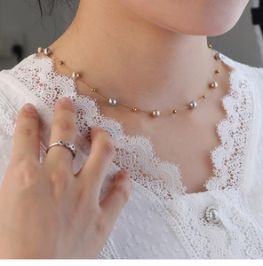 Detail einer mehrfarbigen Perlenkette mit Goldperlen auf einem weißen Spitzen-Outfit