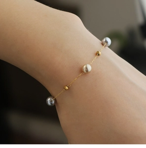 Elegantes Goldkettenarmband mit grauen und cremefarbenen Perlen am Handgelenk eines Models