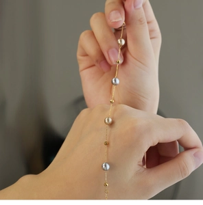 Detail einer eleganten Goldkette mit grauen und Champagner-Perlen an der Hand