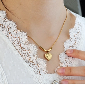 Dettaglio di un ciondolo a cuore vintage placcato oro con trama martellata su catena snake