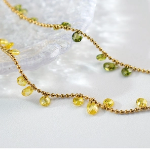 Macro shot of gold beaded chain necklace featuring teardrop green and yellow crystals