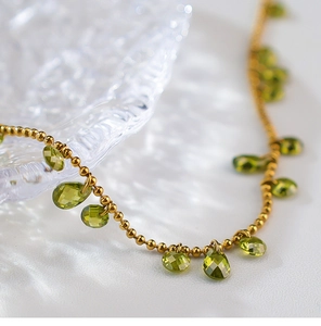 Close-up of golden beaded necklace with faceted olive green teardrop gemstones