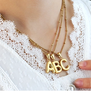 Detailed view of 18K gold plated bubble initial pendants A, B, and C on bead chains