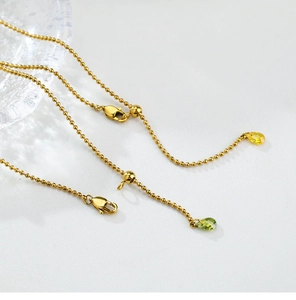 Detailed macro view of golden beaded chain with olive green teardrop crystal pendant