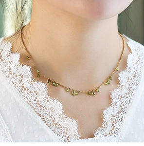 Close-up of olive green teardrop gems on a gold beaded necklace worn by a model