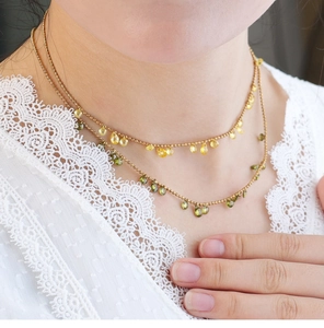 Detail of layered gold beaded necklace featuring olive green and yellow water drop pendants