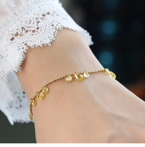 Detail of gold chain bracelet featuring faceted yellow teardrop gemstones on model's wrist
