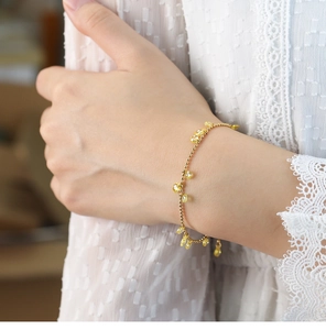 Detail view of a gold beaded bracelet with yellow pear-shaped drop charms on wrist