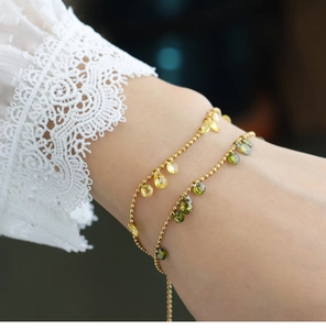 Detail of beaded gold bracelets featuring yellow and olive green teardrop crystals on a wrist
