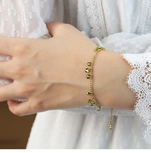 Close-up of olive green teardrop charms on a gold beaded chain bracelet with adjustable link