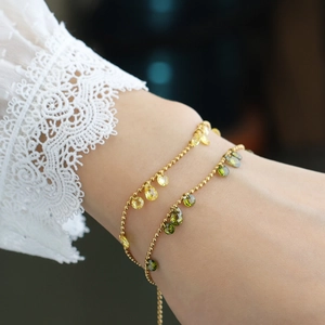 Gold beaded bracelet with olive green and yellow pear-cut gemstone charms on wrist