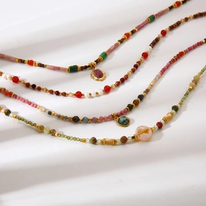 Détail de quatre colliers en pierres naturelles avec pendentifs dorés sur tissu blanc