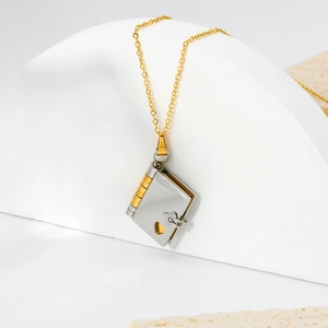Detail of vintage Y2K stainless steel book pendant necklace with heart cutout and gold chain