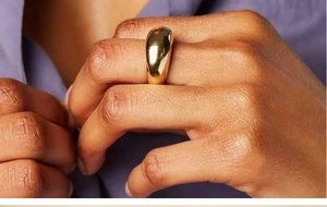 Gros plan d'une bague bombée plaquée or 18 carats sur la main avec un fond violet chic