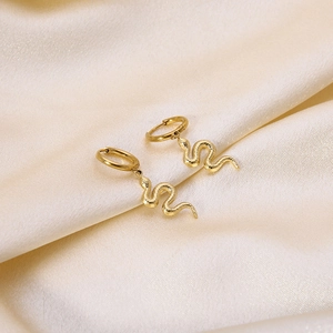 Macro shot of gold-plated snake earrings with scale textures on soft silk fabric