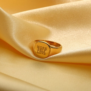 Detailopname van een gouden zegelring met More Self Love gravure op zijde stof