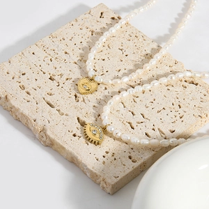 Detail einer Süßwasserperlenkette mit goldenem Herz-Augen-Anhänger auf Steinfläche