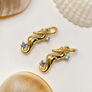 Close-up of gold seahorse charms with blue zircon inlay on white shell background