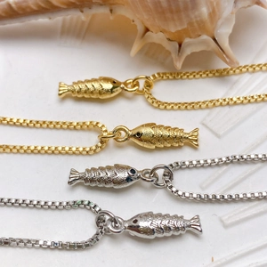 Macro detail of gold and silver fish pendants on box chains with a natural seashell
