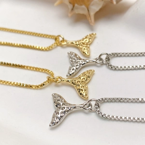 Macro shot of gold and silver fishtail pendants with elegant box chains on a shell background