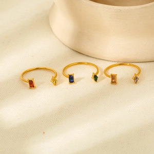 Trois bagues dorées en C avec pierres colorées posées sur un tissu texturé blanc crème