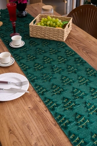 Detail of green plush Christmas table runner with golden embroidery on wood dining table
