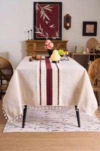 Detail of beige linen tablecloth with wine red striped runner and fringe trim