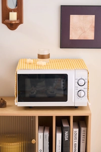 Close-up of yellow checkered microwave dust cover with decorative white pom-pom trim