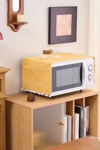Detail of yellow plaid dust cover with pom-pom trim on microwave oven in cozy home setting