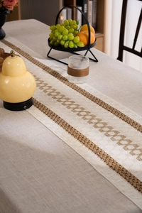 Detailed view of beige linen table runner with brown geometric chain woven patterns