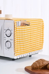 Close-up of yellow plaid dust cover with side storage pocket and white pompom trim
