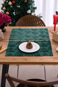 Detail of green Christmas placemats with gold embroidered trees on wooden table