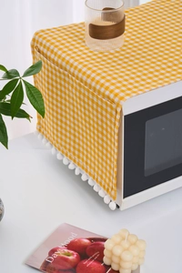 Detailed view of yellow plaid microwave cover with soft white pom-poms and storage pocket