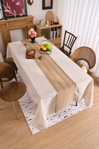 Close-up of linen tablecloth with fringe and woven brown runner in cozy dining setting