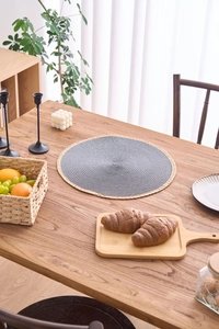 Close-up of woven round placemat with charcoal center and natural fringe on wooden table