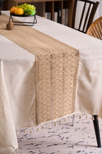 Detail of woven jute table runner with cream fringe tassels on minimalist tablecloth