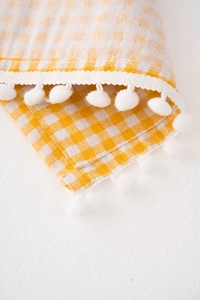 Detail of yellow and white plaid dust cover featuring soft white pom-pom fringe trim