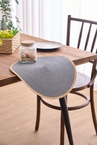 Detail of woven table mat with dark gray center and wood-tone fringe on a dining table