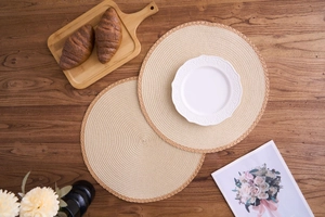 Detail of round woven placemats with brown edges on a wooden table with tableware