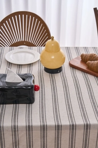 Close-up of yellow gourd lamp and black wavy tissue box on striped cotton linen tablecloth