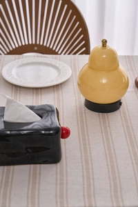 Detail of creative yellow gourd lamp and black tissue box on a striped linen tablecloth