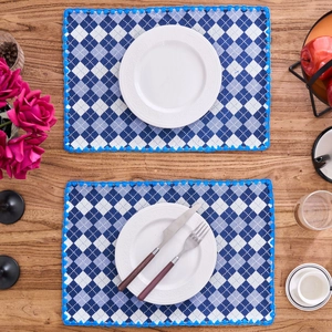 Pair of blue and white checkered jacquard fabric placemats with embroidered edges on wood