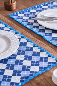 Close-up of blue and white checkered placemats with woven trim on a wooden table